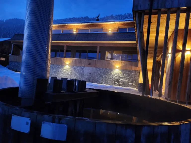 Hot Tub am Alpenchalet in der Winternacht mit beleuchteten Chalets